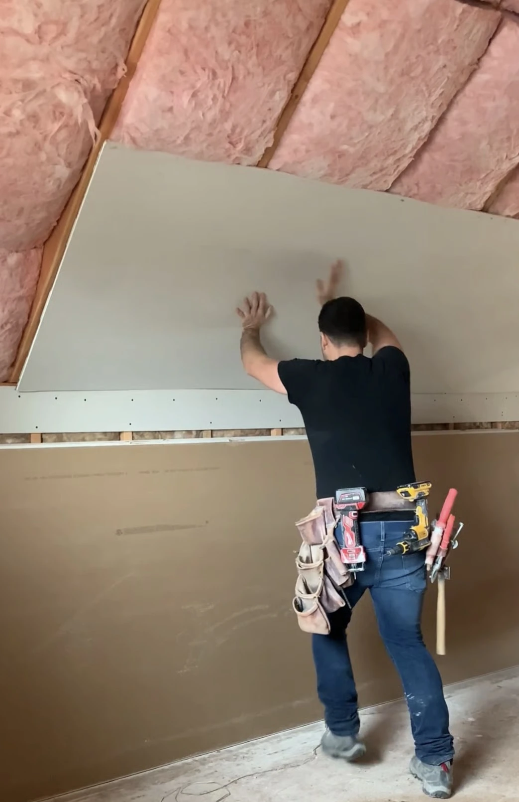 Aesthetic Construction installer positioning a new drywall sheet on an insulated sloped wall